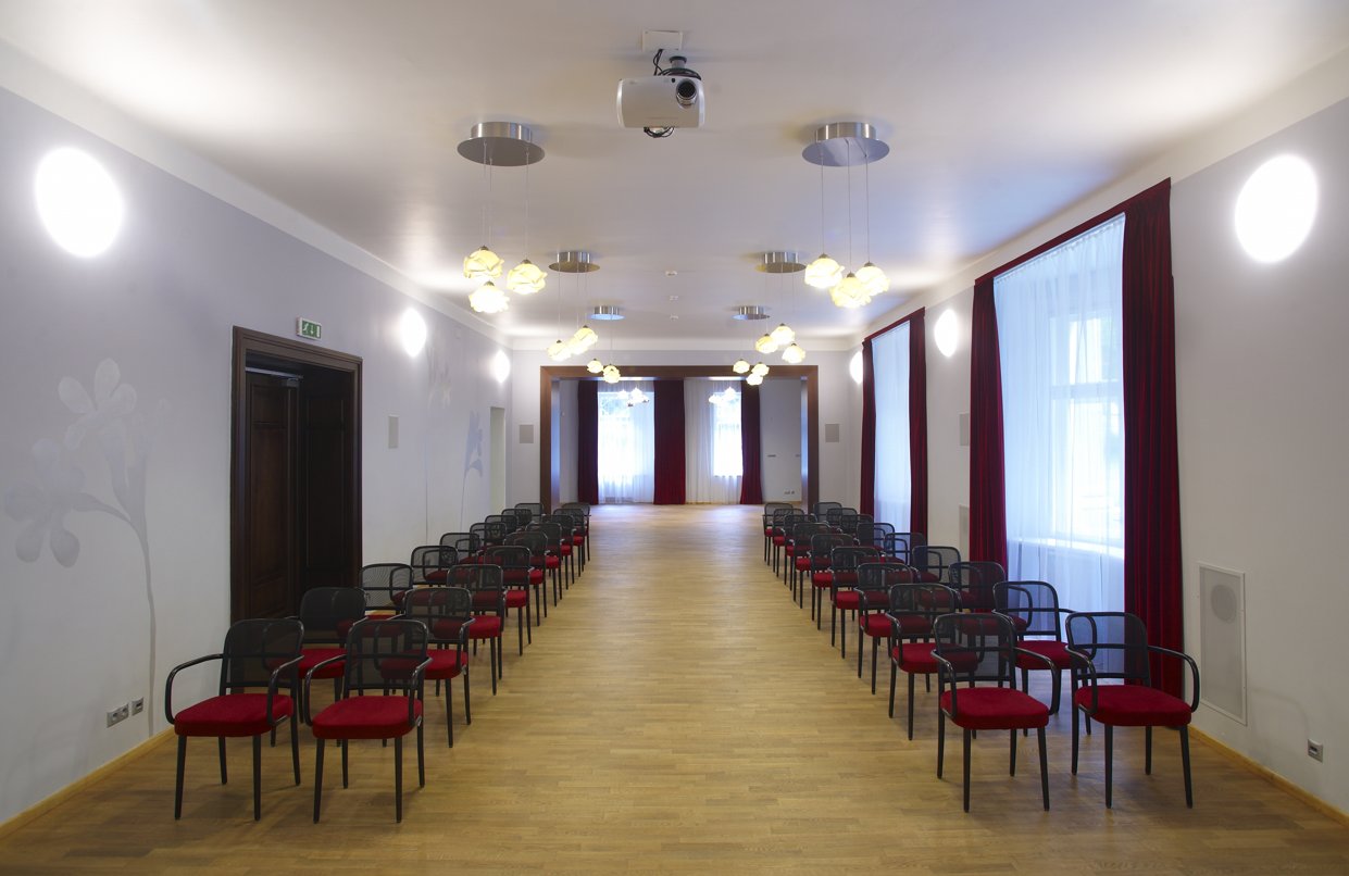 sál s dřevěnou podlahou, po obou stranách 2 řady červených židlí